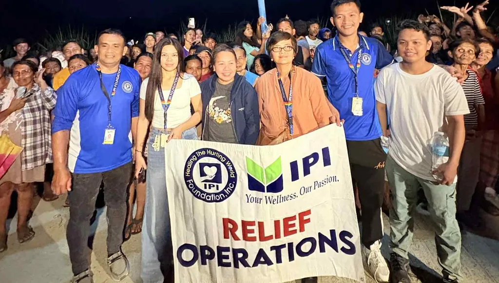 IPI Foundation staff and community members at an evening relief operation, holding a banner reading “Healing The Hurting World — IPI Foundation, Inc.”