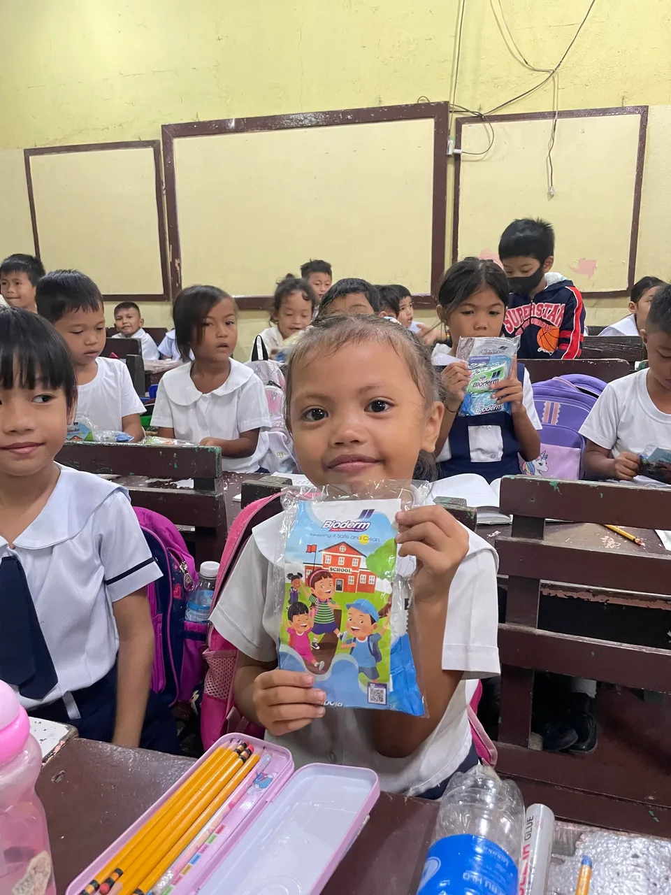 Schoolchildren in their classroom during an IPI Adopt-a-School handwashing and hygiene session, holding the hygiene kits they were given