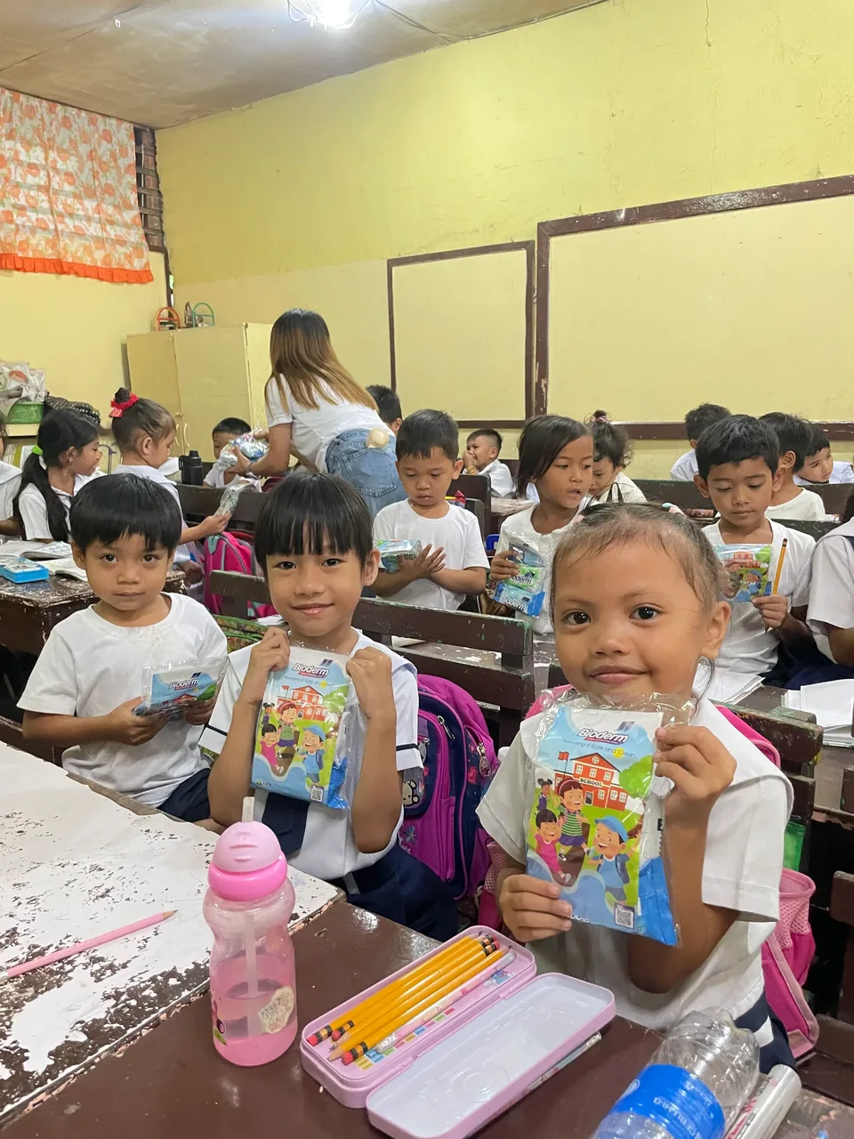 Schoolchildren in their classroom during an IPI Adopt-a-School handwashing and hygiene session, holding the hygiene kits they were given